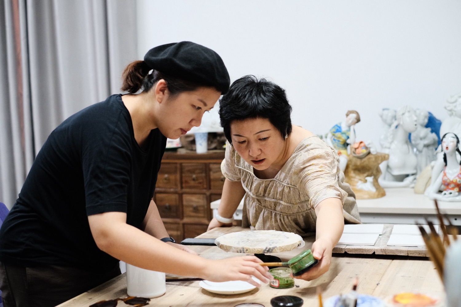 導師手持釉料罐，向 Miko 示範釉上彩的上色技法