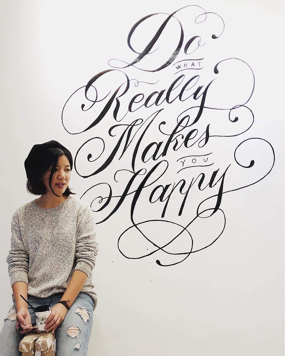 Miko 坐在自己手繪的 Do What Really Makes You Happy 大型牆面字體前
